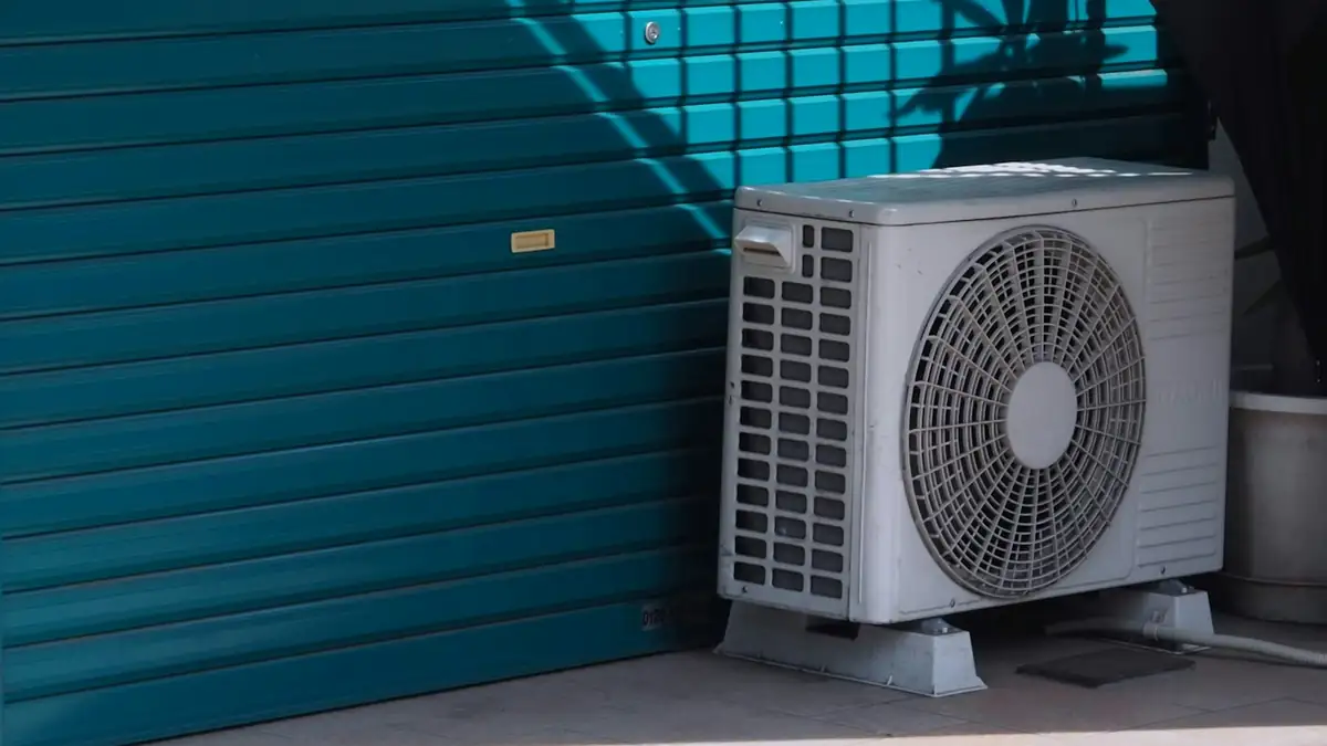 An outdoor air conditioning unit against a blue wall in hard afternoon sun